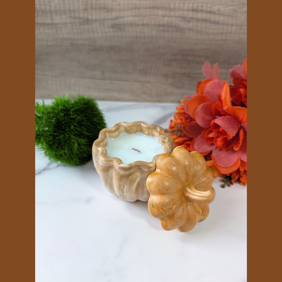 Handcrafted Small Pumpkin Vessel in orange inside of the vessel is fill with coconut apricot wax in front of falls flowers, green moss in top of white countertop