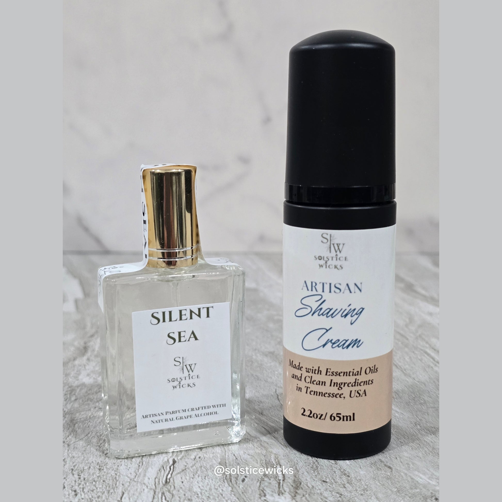 Two bottles of 'Silent Sea' perfume and 'Artisan Shaving Cream' on a marble surface.