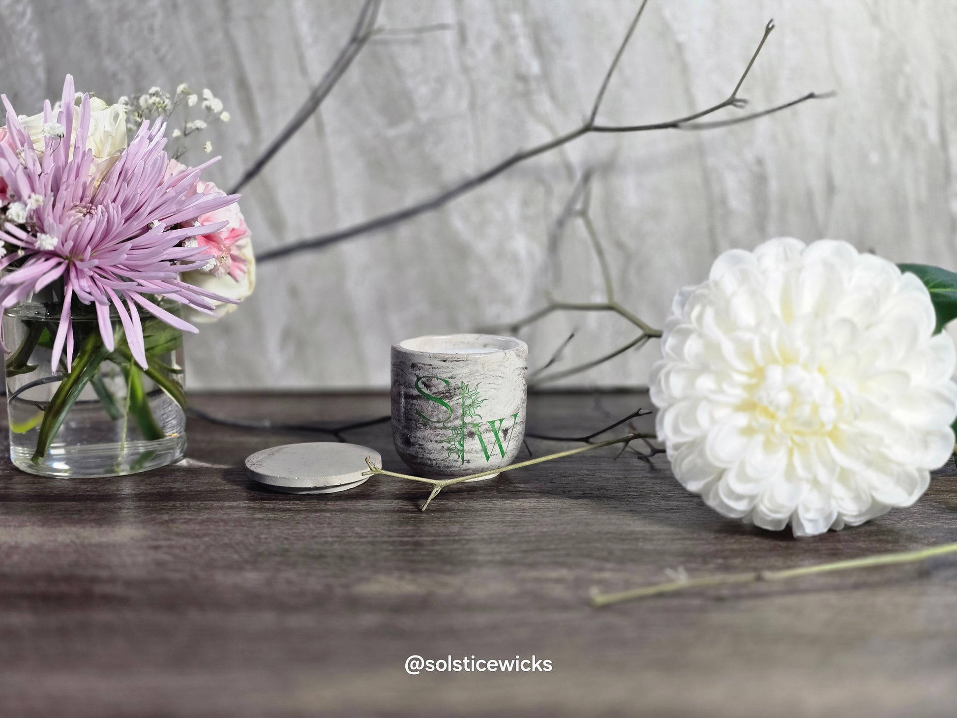Candle with floral design on a wooden surface with flowers and branches.