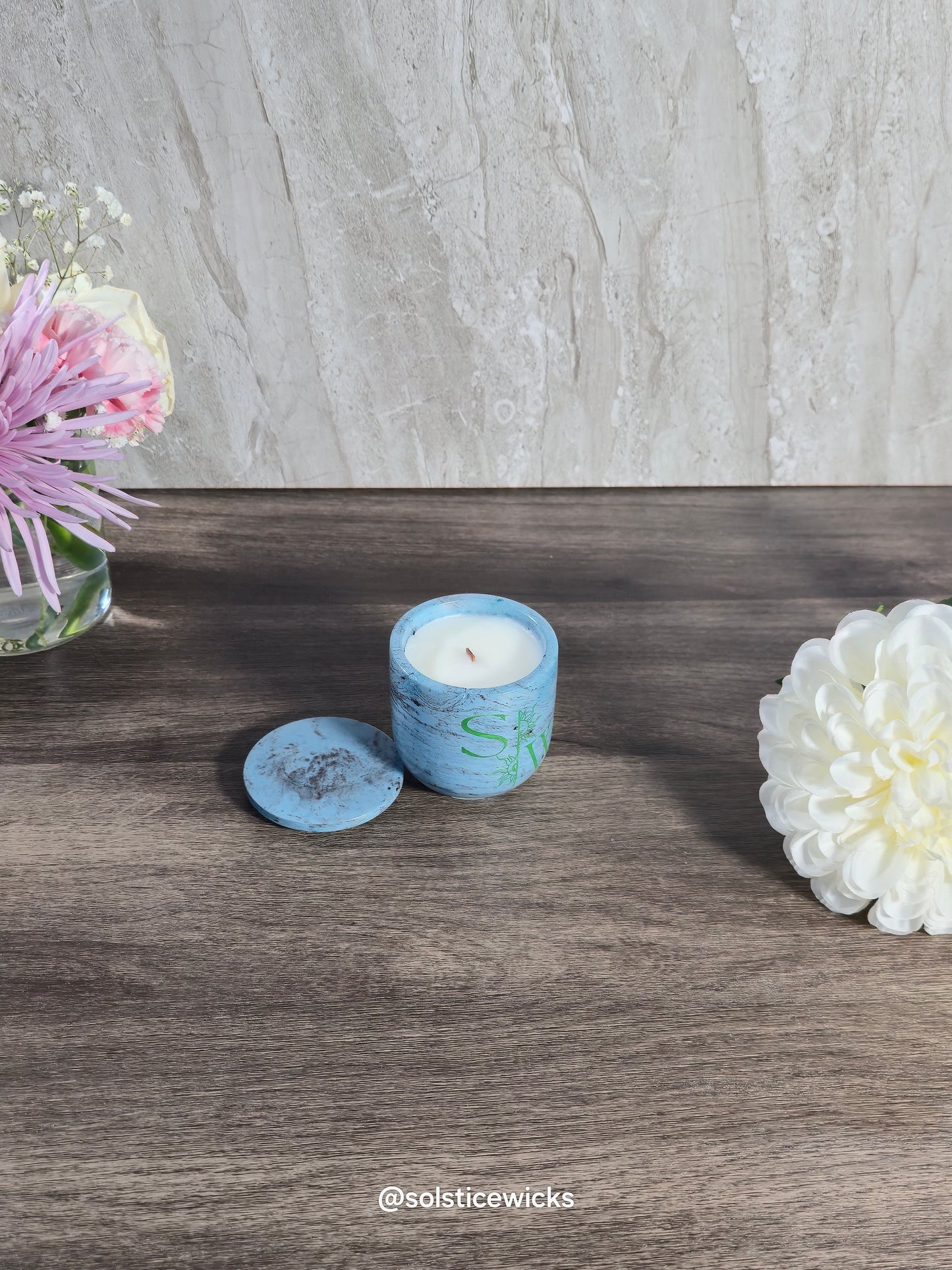 Blue candle with decorative design on a wooden surface with flowers.