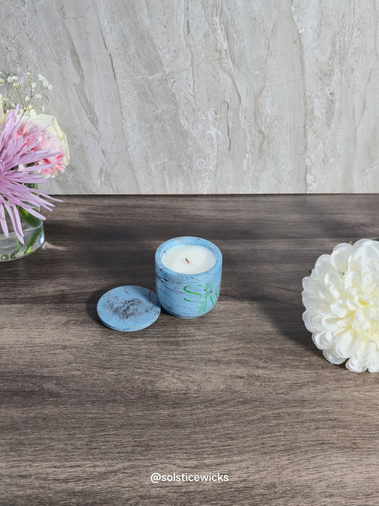 Blue candle with decorative design on a wooden surface with flowers.
