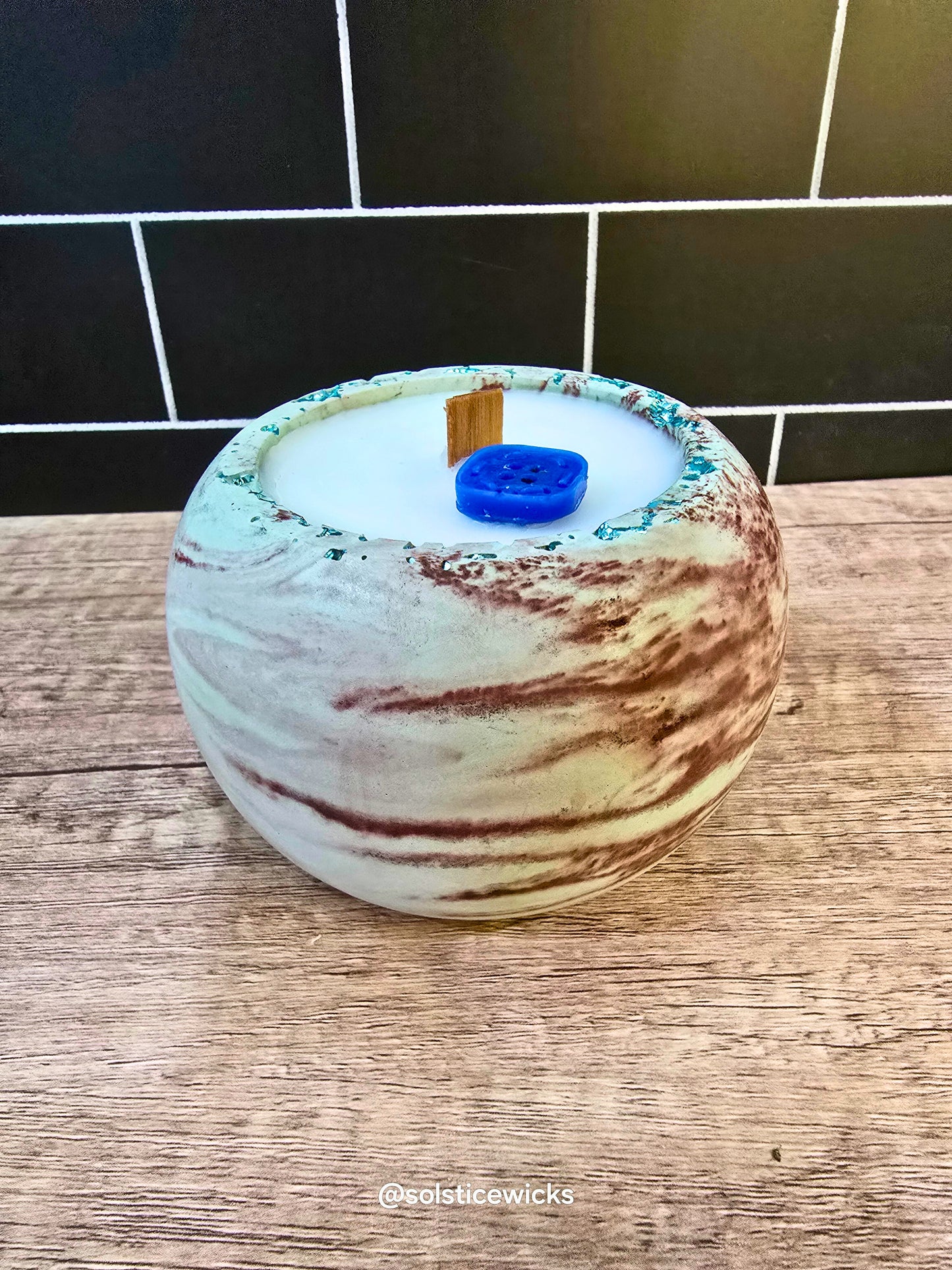 Marbled candle with a blue wick on a wooden surface. Earthbound Calm Candle in concrete jar – mint, citrus, and herbal notes for a calming, fresh home scent.