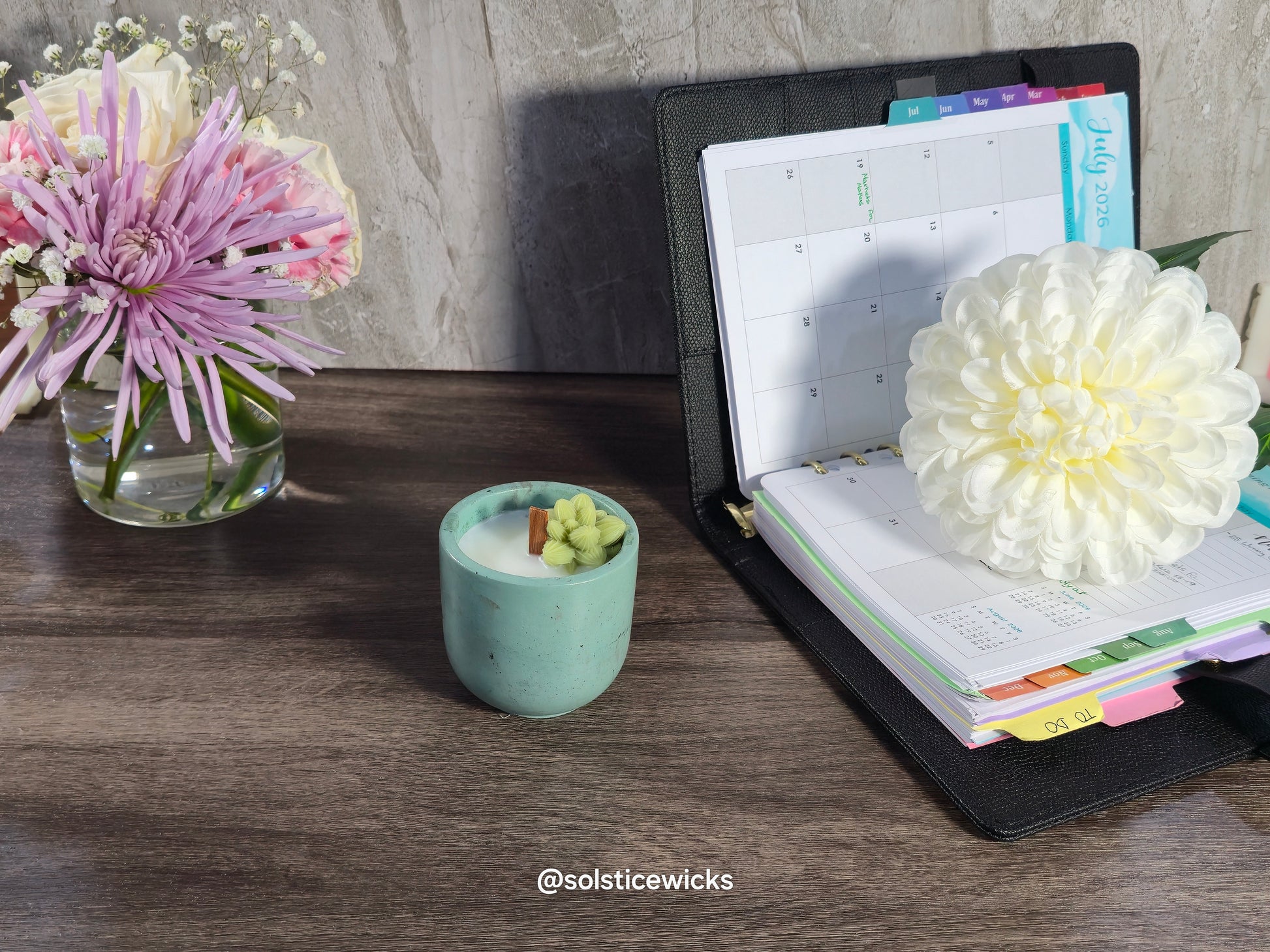Desk with a planner, candle, and flowers on a wooden surface